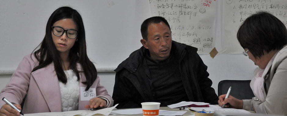 A Chinese factory worker talks while women either side of him take notes