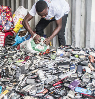 A man gathers up scrap mobile phones from a large pile on the ground