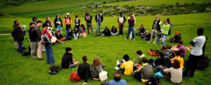 A group of people in a circle hold a group discussion outside
