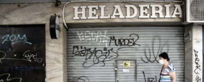 a woman in a mask walks in front of a shuttered storefront in Buenos Aires
